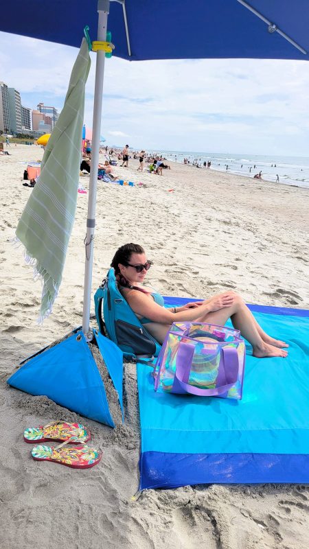 Girl sitting on the beach surrounded by beach accessories
