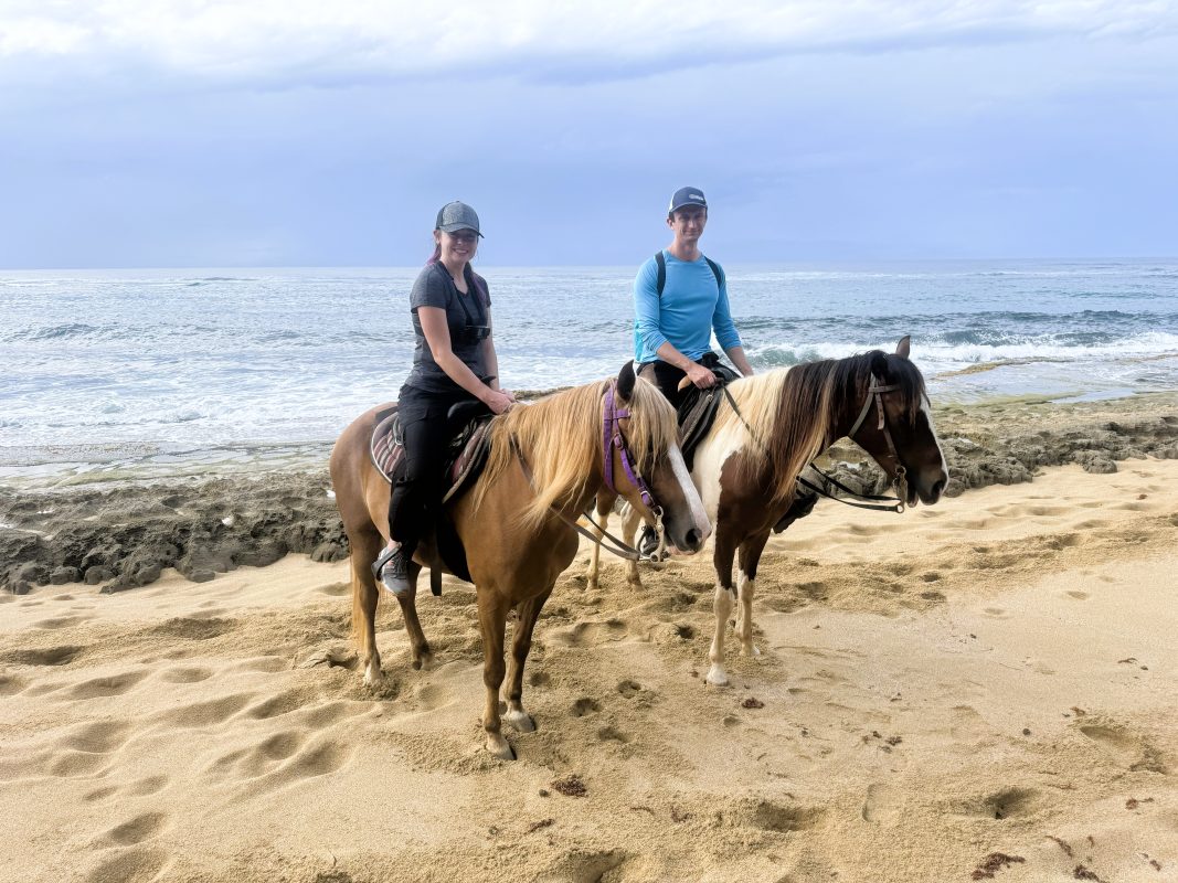 man and woman riding horses on the beach